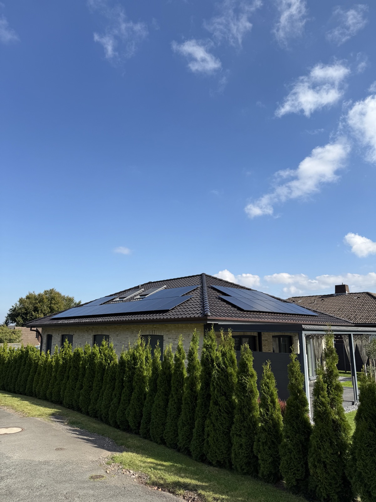Referenzanlage einer Familie aus der Region — Wohnhaus mit Hecke und schwarzer Photovoltaik-Anlage